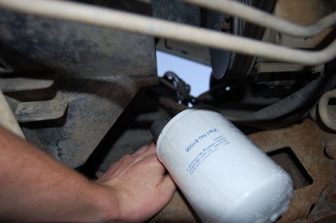 1994 Ford Bronco - A bare hand threading a white spin-on oil filter marked Part No 81008 onto the engine from underneath the vehicle during an oil change. The…