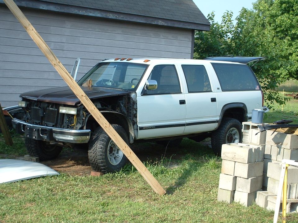 White Chevy Suburban SUV mid-restoration with front clip removed by barn