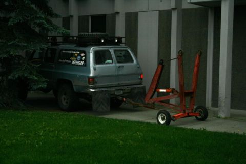 1990 Chevrolet Suburban - This older model SUV is equipped with a roof rack and a spare tire, and is hitched to a red trailer.