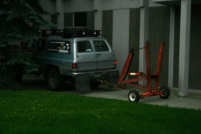 Blue SUV with roof rack and spare tire, towing a red trailer