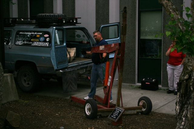 Blue Chevrolet K5 Blazer with roof rack, spare tire, and stickers on the side. A man is loading items into the open rear