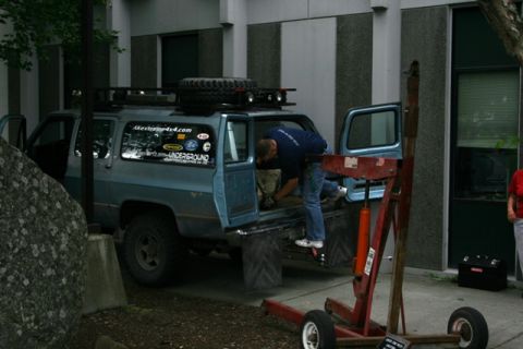 1990 Chevrolet Suburban - A person is loading items into the back of a blue SUV, which has a spare tire mounted on its roof rack.