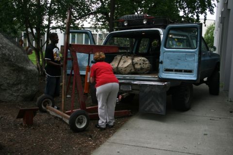 1990 Chevrolet Suburban - A light blue SUV is being loaded with a large rock, with two people assisting.