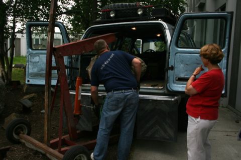 1990 Chevrolet Suburban - A man uses an engine hoist to load a large item into the back of a light blue SUV while a woman observes.