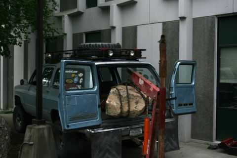1990 Chevrolet Suburban - A blue SUV is parked outside a building, with its rear doors open, revealing a large rock secured by chains.