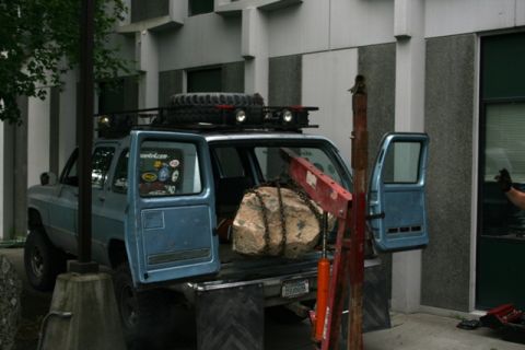 1990 Chevrolet Suburban - A blue 1990 Chevrolet Suburban is loaded with a large rock and a crane, with its rear doors open.