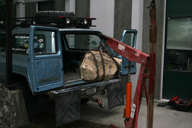 Blue 1990 Chevrolet Suburban, rear view, with doors open, a rock suspended by chains, and a red engine hoist