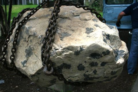 1990 Chevrolet Suburban - A large rock is being moved by chains, with a blue vehicle and a person visible in the background.