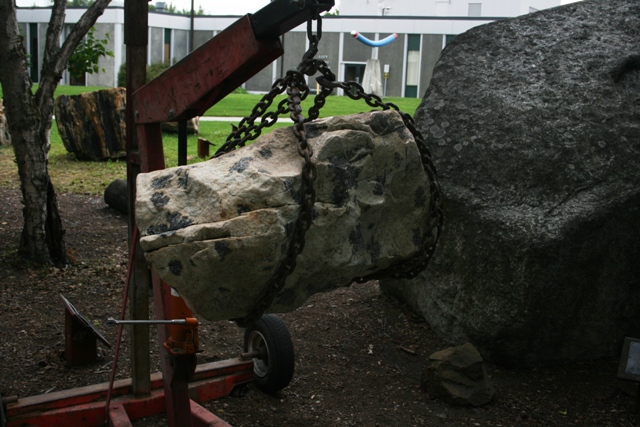 Rock being lifted by a red crane with chains