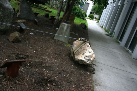 1990 Chevrolet Suburban - A large rock is being moved with a cable and straps, positioned on a dirt area beside a concrete walkway and building.