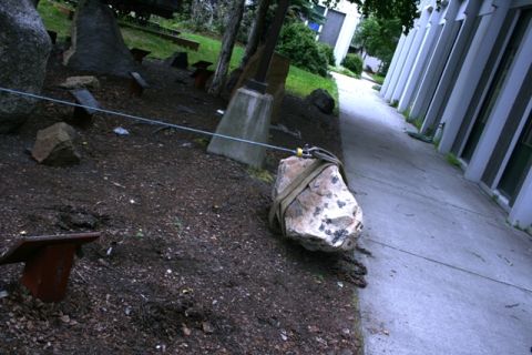 1990 Chevrolet Suburban - A rock is being moved using straps and a cable, next to a building and walkway.