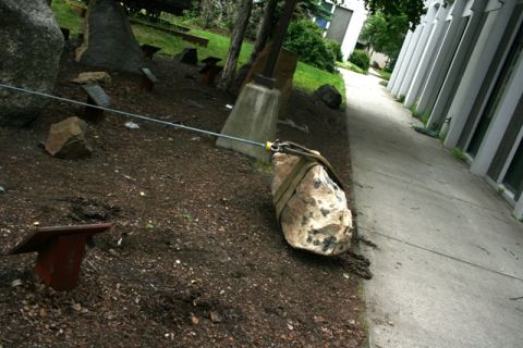 1990 Chevrolet Suburban - A large rock is secured with straps and a cable, positioned on a dirt area next to a paved walkway.