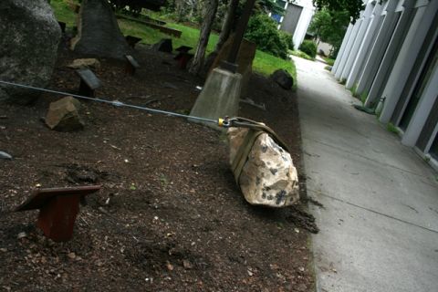 1990 Chevrolet Suburban - An outdoor rock garden display features large stones secured by cables, adjacent to a modern building with a paved walkway.