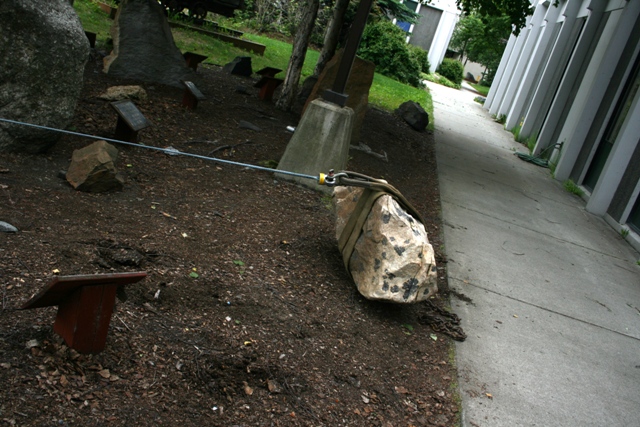 Rock garden with large stones, metal cables, and concrete pillars next to a building