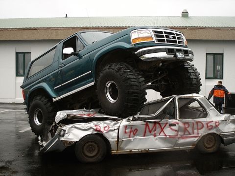 1996 Ford Bronco - A green 1996 Ford Bronco is positioned on top of a heavily damaged silver car.