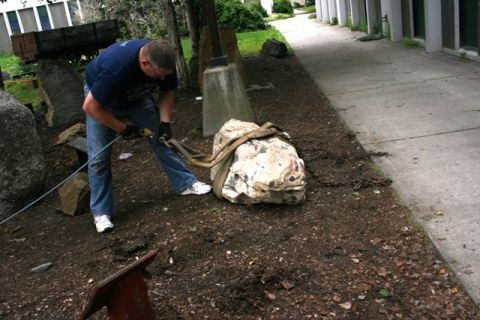 1990 Chevrolet Suburban - A man is using straps and a chain to move a large rock in a garden area.