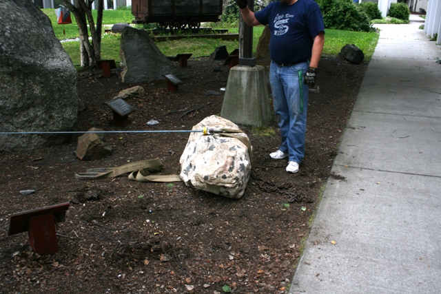 Man standing next to a large rock being moved with chains and straps