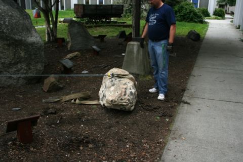 1990 Chevrolet Suburban - A man is using a cable and straps to move a large rock in an outdoor area with some large boulders and informational plaques.