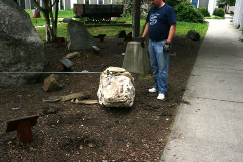1990 Chevrolet Suburban - A man stands in a rock garden exhibit, near a large rock covered in a tarp and surrounded by chains.