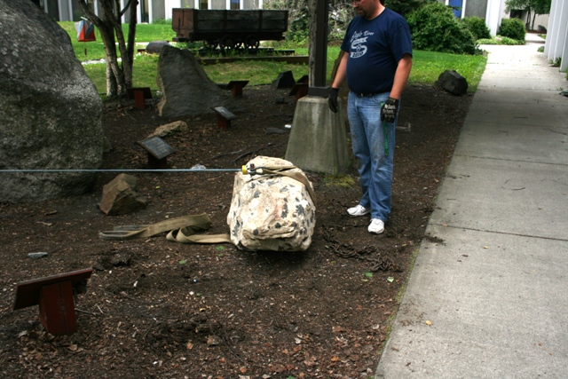 Rock garden scene with a man standing next to a large, tarp-covered rock