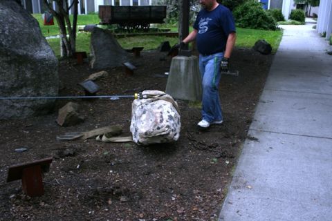 1990 Chevrolet Suburban - A man is using straps and chains to move a large, rough-surfaced rock in an outdoor area with other large rocks and some old train cars in…