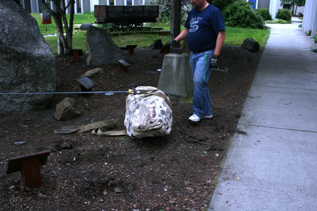 man in blue shirt and jeans moving a large rock with a strap and chains