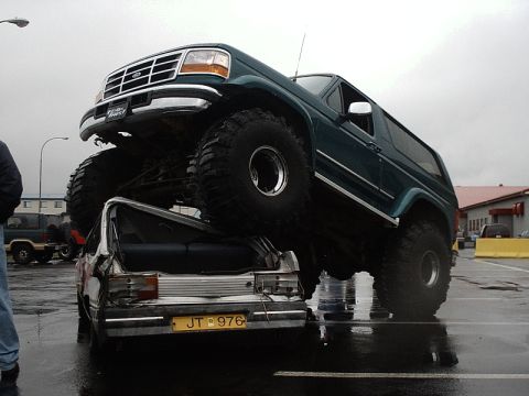 1996 Ford Bronco - A modified 1996 Ford Bronco is shown crushing a smaller vehicle, likely at a show or event.