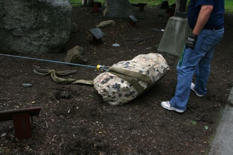 1990 Chevrolet Suburban - A man is using a strap and winch to move a large rock. The scene appears to be outdoors in a park or garden area.