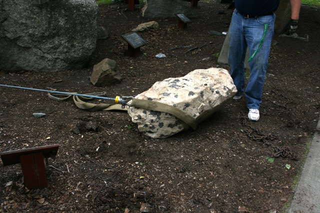 Rock being moved with a strap and cable, person in jeans nearby