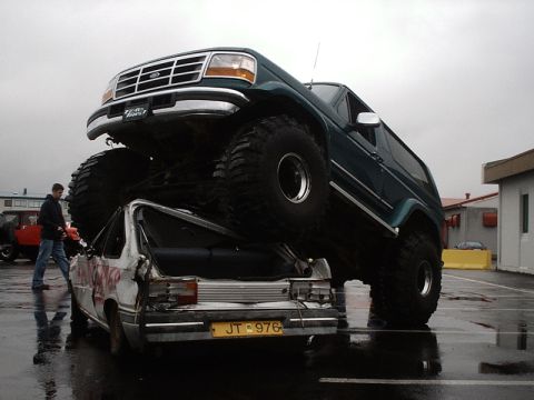1996 Ford Bronco - A 1996 Ford Bronco monster truck is shown crushing a car, with a person standing nearby.