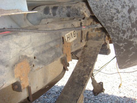 Close-up of rusted frame rail with a label reading 'BVH'. Leaf spring and suspension parts are visible