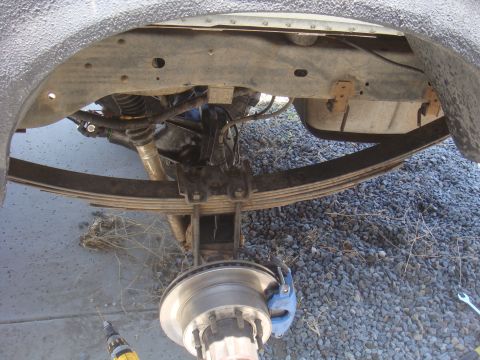 Rear axle assembly with leaf springs, brake caliper, and hub. Textured fender liner above