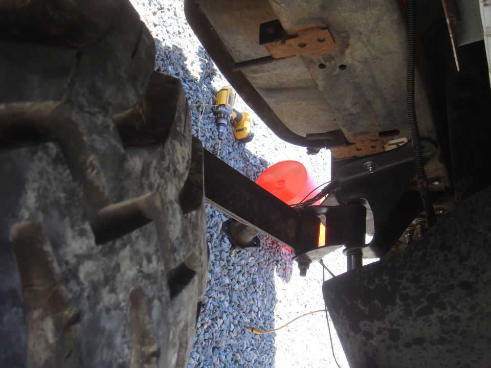 Undercarriage view of a vehicle's suspension and large tire. Supermotors.net logo visible