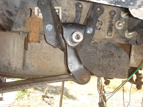 Close-up of a black metal suspension component attached to a rusty frame with bolts and a nut