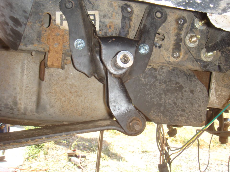 Close-up of a black metal suspension component attached to a rusty frame with bolts and a nut