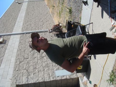 Man in a camouflage hat and green t-shirt stands outdoors, pointing with his left hand