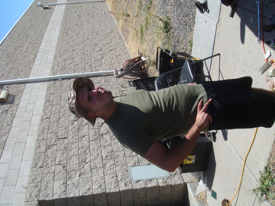 Man in a camouflage hat and green t-shirt stands outdoors, pointing with his left hand