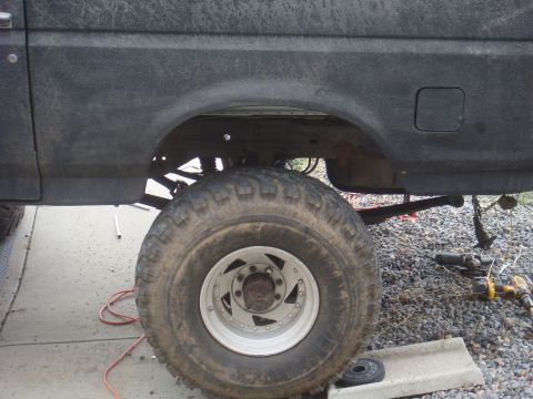 Side view of a lifted Ford Bronco's rear wheel well and tire. Tools are on the ground nearby