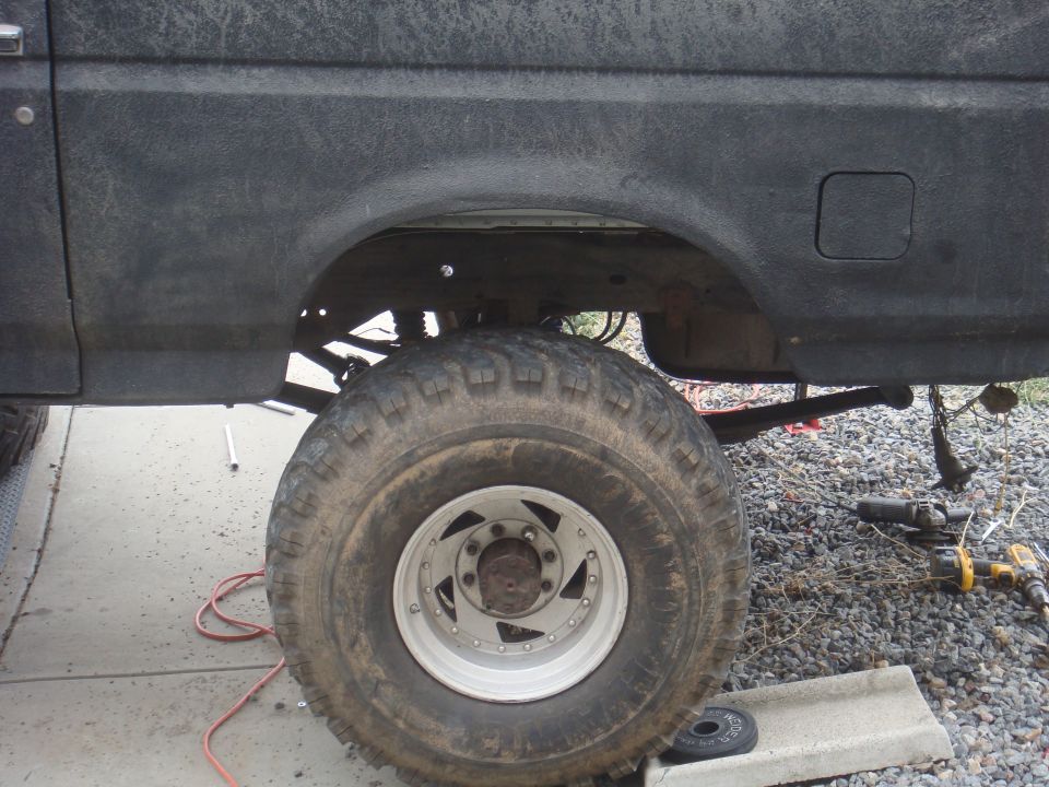Side view of a lifted Ford Bronco's rear wheel well and tire. Tools are on the ground nearby