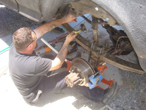Man with hammer working on vehicle's rear axle and suspension components