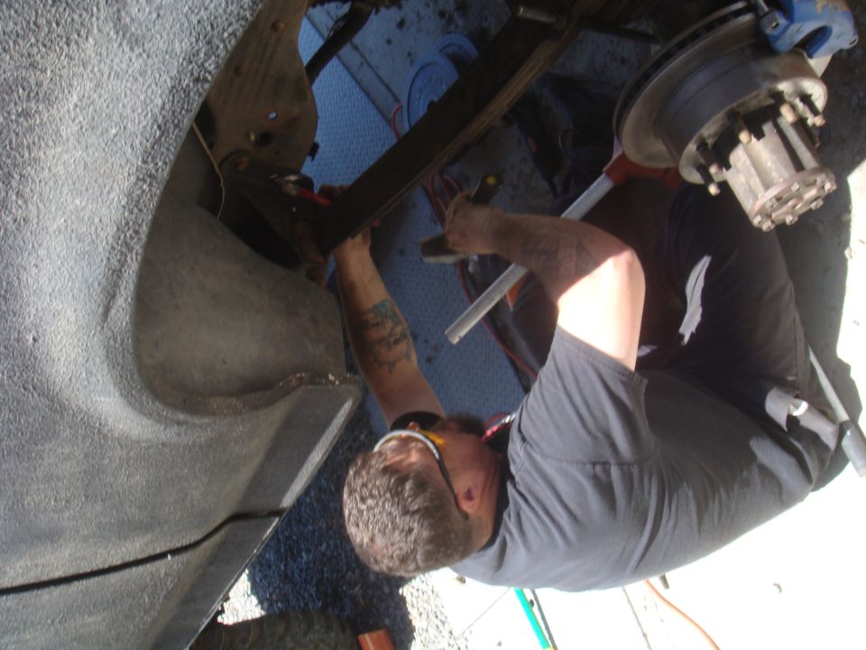 Mechanic working on the suspension and brake assembly of a vehicle. The wheel hub is visible