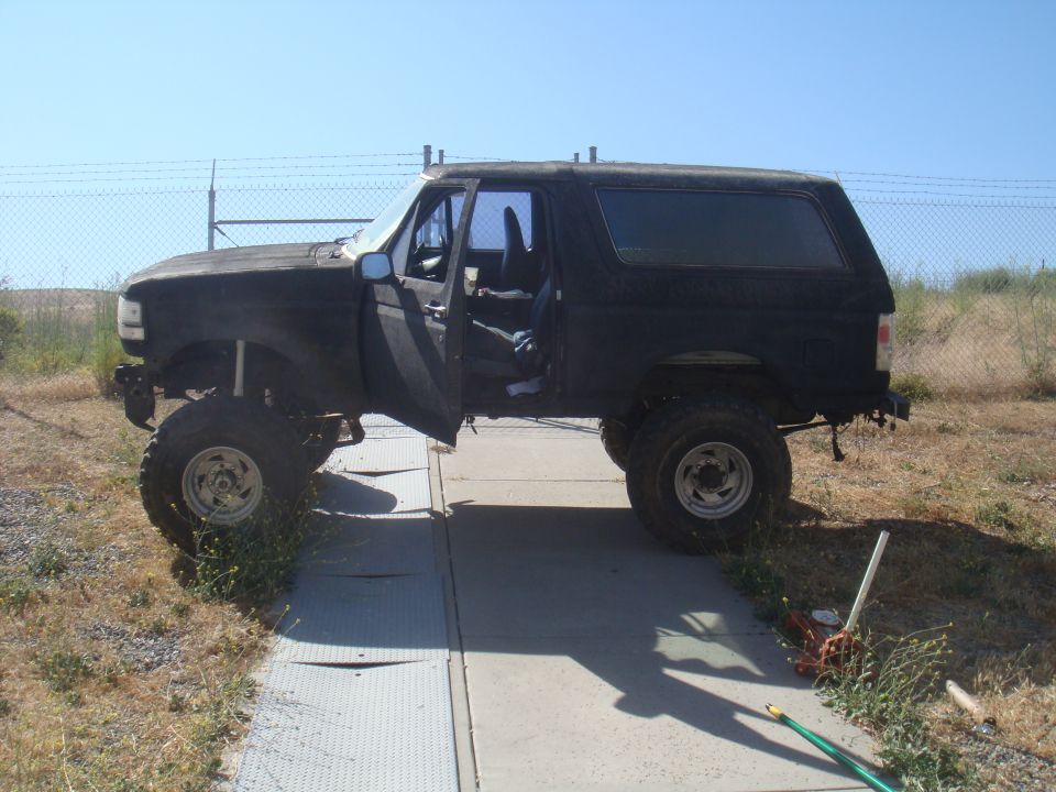 Black 1992 Ford Bronco with doors open, lifted suspension, and large tires parked on a concrete pad