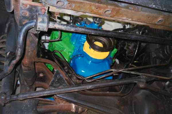 View from under a vehicle showing a blue and green painted engine block amid rusty frame and steering parts