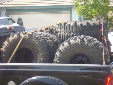 Four large off-road tires strapped in the bed of a black pickup truck