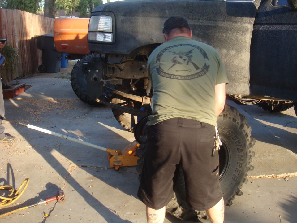 Black truck front end being serviced with a jack; orange truck in background