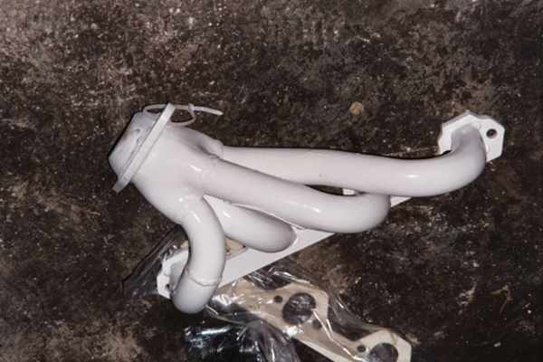 White ceramic-coated exhaust header lying on concrete floor with wrapped gasket underneath