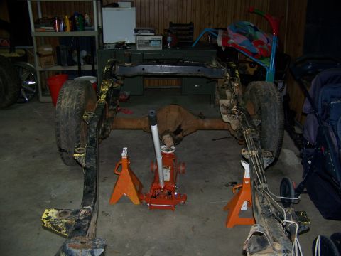 1992 Jeep YJ - The frame and axles of a 1992 Jeep YJ are visible, supported by jack stands in a garage.