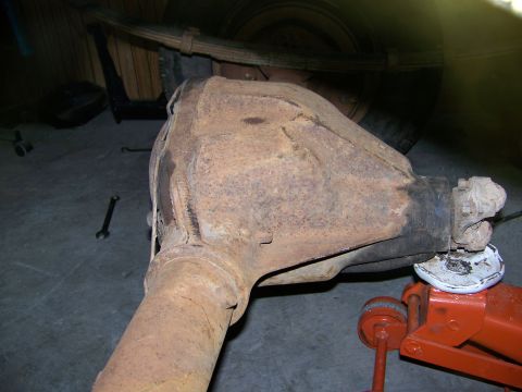1992 Jeep YJ - A rusty rear axle assembly is supported by an orange hydraulic jack on a concrete floor.