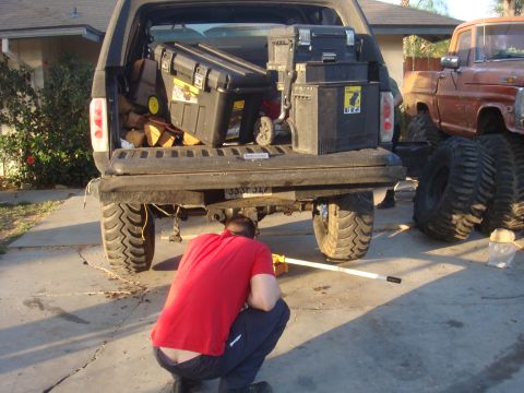 Black Ford Bronco rear view with toolbox and wood in bed, orange truck with large tires beside it