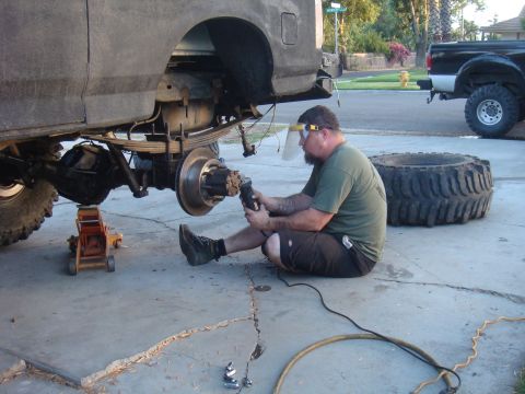 Man grinding on rear axle of vehicle, another truck in background